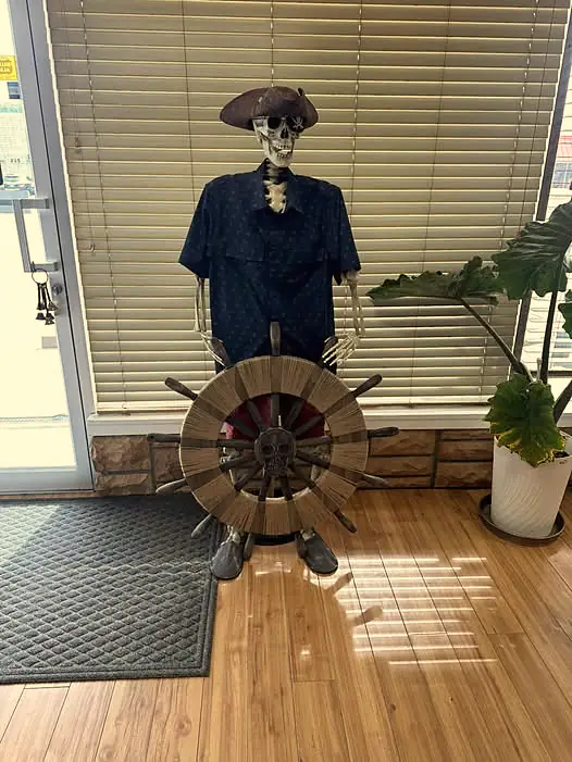 A skeleton pirate in a captain’s hat greeting shoppers at the door, behind a ship’s wheel